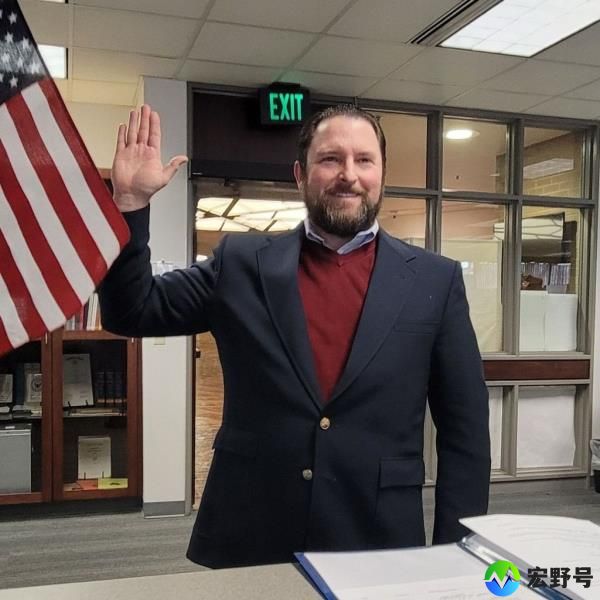Utah State Representative Brett Garner raising his right hand, while standing in front of an American flag.