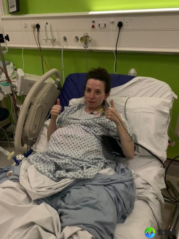 Kat Romero in a hospital bed, with various tubes attached to her, giving a thumb