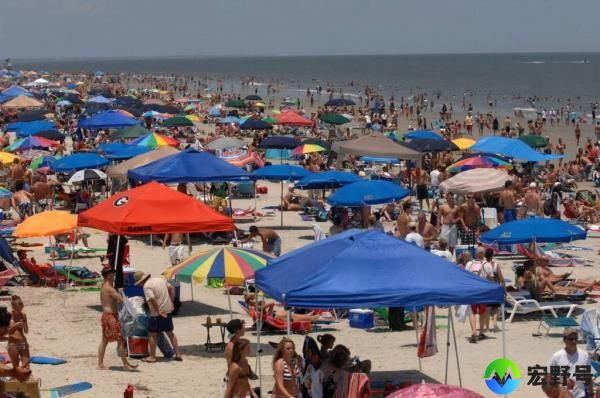 Crowded beach on Independence Day with beachgoers and packed tents, people using umbrellas under hot and humid weather conditions