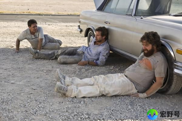 Ed Helms, Bradley Cooper, and Zach Galifianakis leaning against a car. 